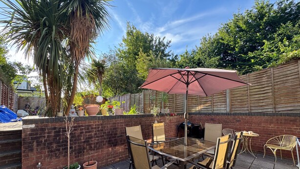 Een terras buiten met een glazen tafel, stoelen en een grote parasol.