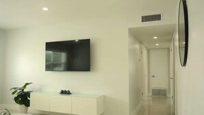 Una sala moderna con un televisor de pantalla plana montado en la pared, una consola blanca y una planta en maceta.