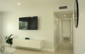 Ein modernes Wohnzimmer mit flachbildfernseher an der Wand, einem weißen Konsolentisch und einer Zimmerpflanze.