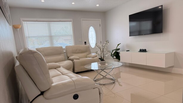 Una sala moderna con un sofá modular, una mesa de centro de vidrio, un televisor de pantalla plana y un mueble blanco.