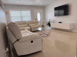 Un salon moderne avec un canapé d’angle, une table basse en verre, un téléviseur à écran plat et un meuble blanc.