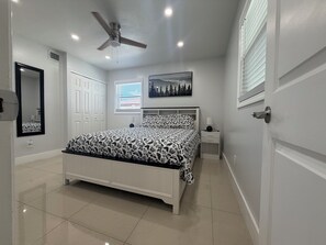 A bedroom with a bed, a ceiling fan, a nightstand, a wall-mounted lamp, and a window with blinds. - Spacious 3-Bedrooms. Home in Tampa. Fast WiFi & Free Parking (Tampa)