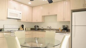 Una cocina moderna con armarios de madera clara, una mesa de comedor de vidrio y electrodomésticos blancos.