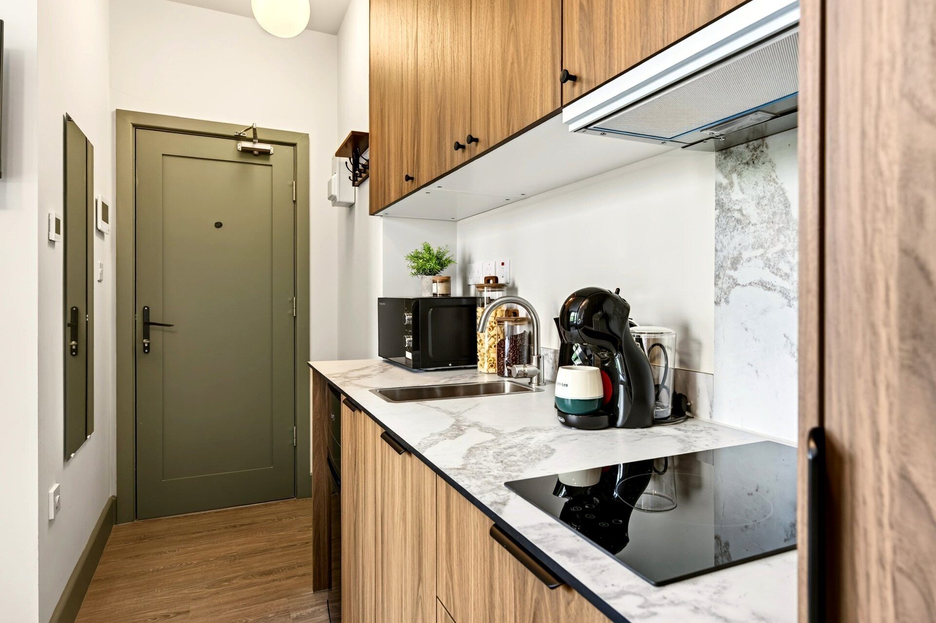 Een compacte keuken met een inbouwfornuis, een koffiezetapparaat en een spoelbak.