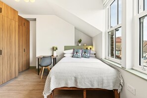 A bedroom with a bed, a desk, a chair, a window, and a wardrobe. - GuestReady - Studio w Kitchenette in Harrow (London)
