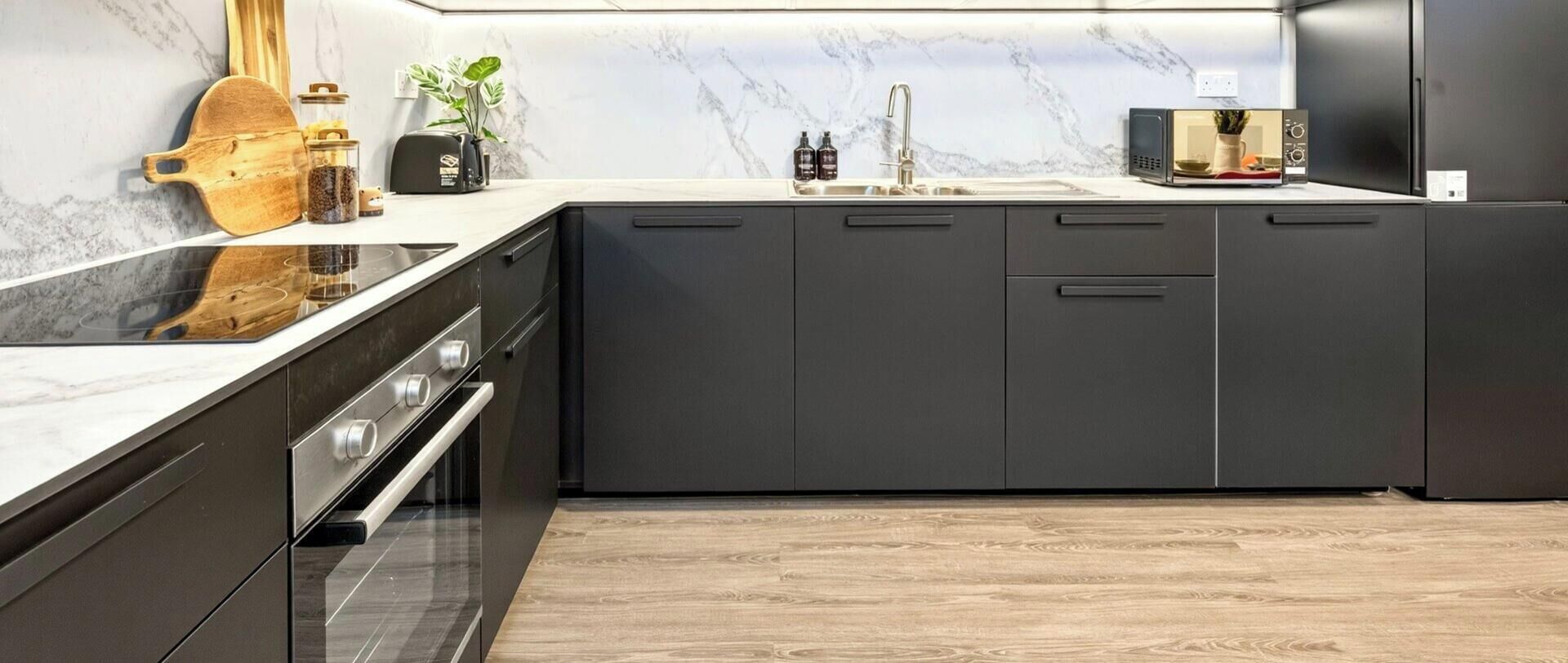 Cocina moderna con armarios oscuros, horno empotrado y salpicadero de mármol.