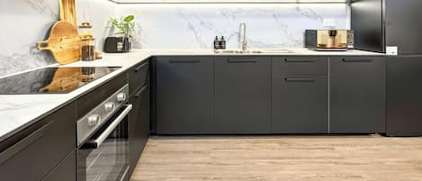 Cocina moderna con armarios oscuros, horno empotrado y salpicadero de mármol.