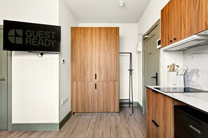 A modern kitchen with wooden cabinets, a built-in oven, and a 'GUEST READY' sign. - GuestReady - Trendy Studio in Harrow (London)