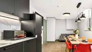 A modern kitchen with a built-in microwave, a dining area with a wooden table and red chairs, and a grey sofa in the background. - GuestReady - Trendy Studio in Harrow (London)