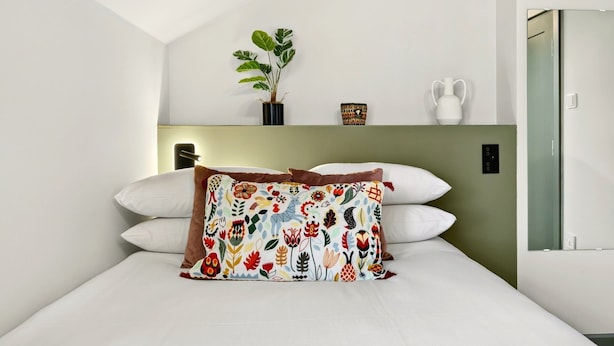 A neatly arranged hotel room with a bed, a bedside table, a potted plant, and a small decorative item on the wall. - GuestReady - Trendy Studio in Harrow (London)