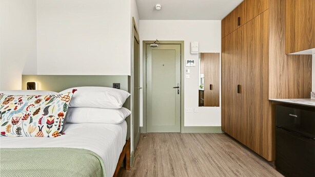 Un dormitorio con cama, mesita de noche, armario y una pequeña cocina.