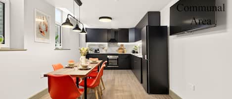 A modern kitchen with black cabinets, a dining table with orange chairs, and a sign indicating a communal area.