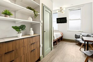 A modern room with a wooden cabinet, a bed, a desk with a chair, and a TV on the wall. - GuestReady - King Studio w Kitchenette in Harrow (London)