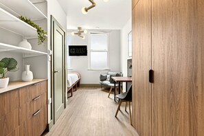 A modern, compact room with a bed, a desk, a chair, a wooden wardrobe, and a 'GUEST READY' sign. - GuestReady - King Studio w Kitchenette in Harrow (London)