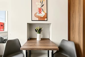 Ein zeitgemäßer Essbereich mit Holztisch, zwei Stühlen, einer weißen Vase mit Blumen und einem gerahmten Kunstwerk darüber.