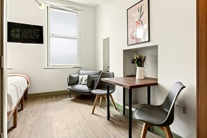 Ein Zimmer mit einem Bett, einem grauen Sofa, einem kleinen Tisch mit einer Vase und einem Schild mit der Aufschrift 'GUEST READY'.