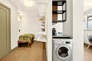 Ein kleines Zimmer mit Bett, Waschmaschine und einer kompakten Küchenzeile.