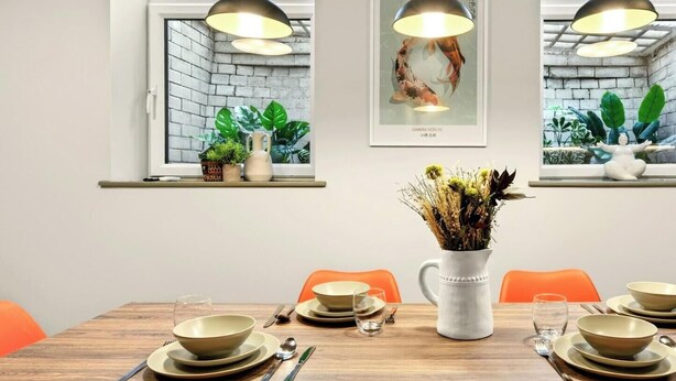 A dining area with a wooden table set for four, orange chairs, and pendant lighting. - GuestReady - Large Studio w Kitchen in Harrow (London)