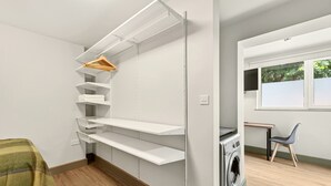 A laundry room with a washing machine, a chair, and a window with a view of greenery. - GuestReady - Large Studio w Kitchen in Harrow (London)