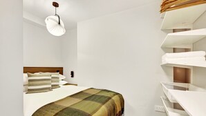 A bedroom with a bed, a bedside table, a wall-mounted shelf with towels, and a hanging light fixture. - GuestReady - Large Studio w Kitchen in Harrow (London)