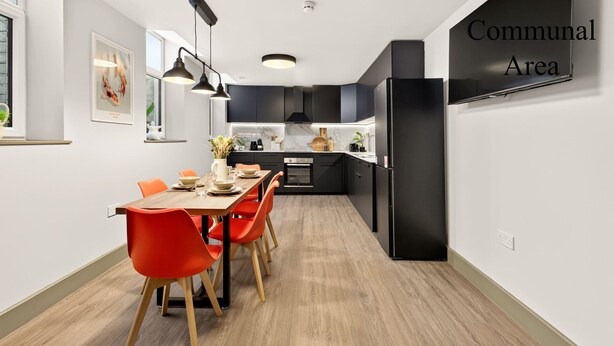 A modern kitchen with black cabinets, a dining table with orange chairs, and a sign indicating a communal area. - GuestReady - Contemporary King Studio in Harrow (London)