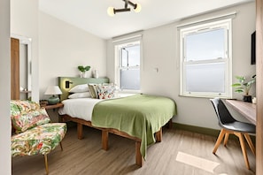 Ein Schlafzimmer mit Bett, Schreibtisch, Stuhl und Fenster.