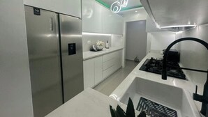 Una cuina moderna amb electrodomèstics d'acer inoxidable, armaris blancs i una cuina de gas.