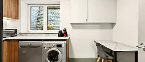 A compact kitchen with a washing machine, a coffee maker, and a small dining area.