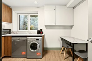 A compact kitchen with a washing machine, a coffee maker, and a small dining area. - GuestReady - Modern 1BR w Full Kitchen in Harrow (London)