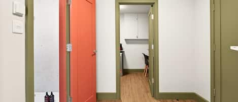 A narrow hallway with a wooden floor, a red door on the left, and a green door on the right.