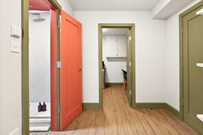A narrow hallway with a wooden floor, a red door on the left, and a green door on the right. - GuestReady - Modern 1BR w Full Kitchen in Harrow (London)