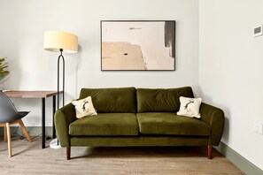 Ein grünes Sofa mit zwei Zierkissen, einer Stehlampe und einem gerahmten abstrakten Gemälde an der Wand.