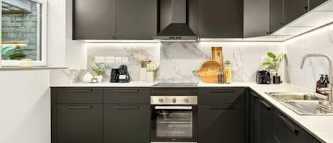 A modern kitchen with dark cabinetry, a built-in oven, and a marble countertop.