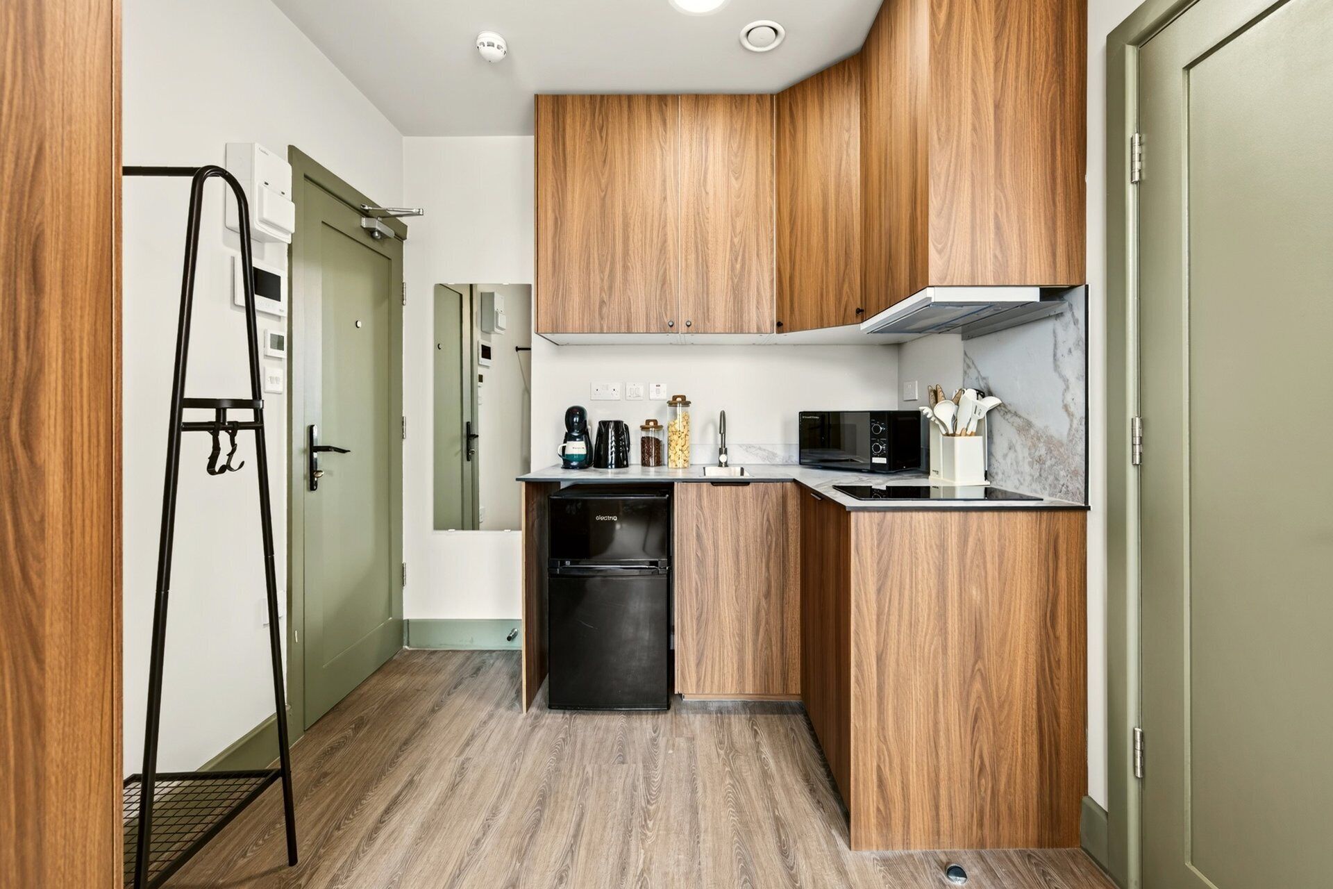 Una cocina compacta con armarios de madera, un refrigerador negro, un microondas y un lavamanos pequeño.