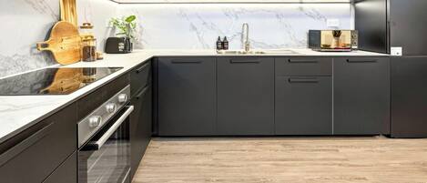 A modern kitchen with dark cabinetry, a built-in oven, and a marble backsplash.