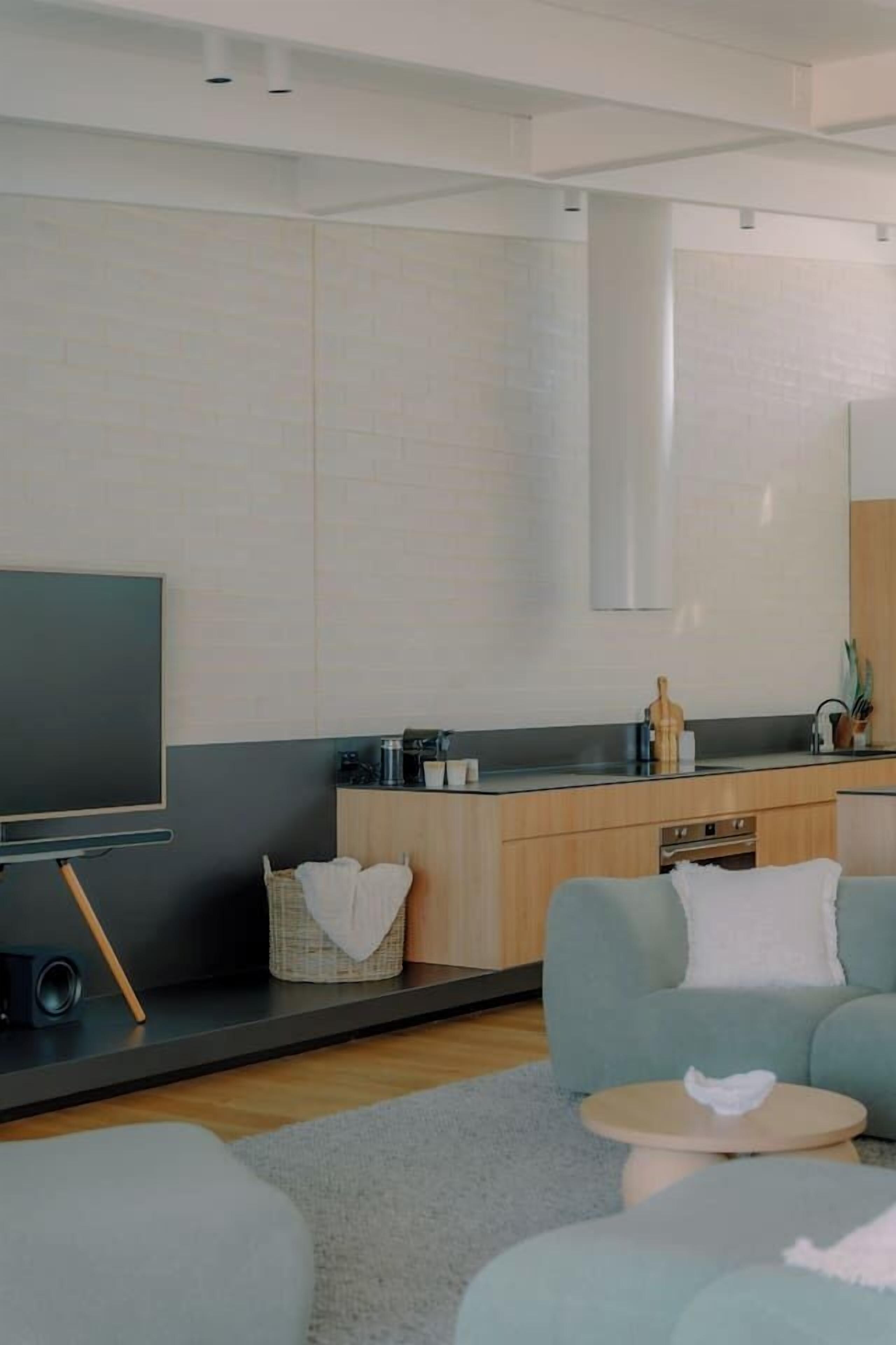 A modern living room with a flat-screen TV, a sofa, a coffee table, and a kitchen area with a counter and cabinets.