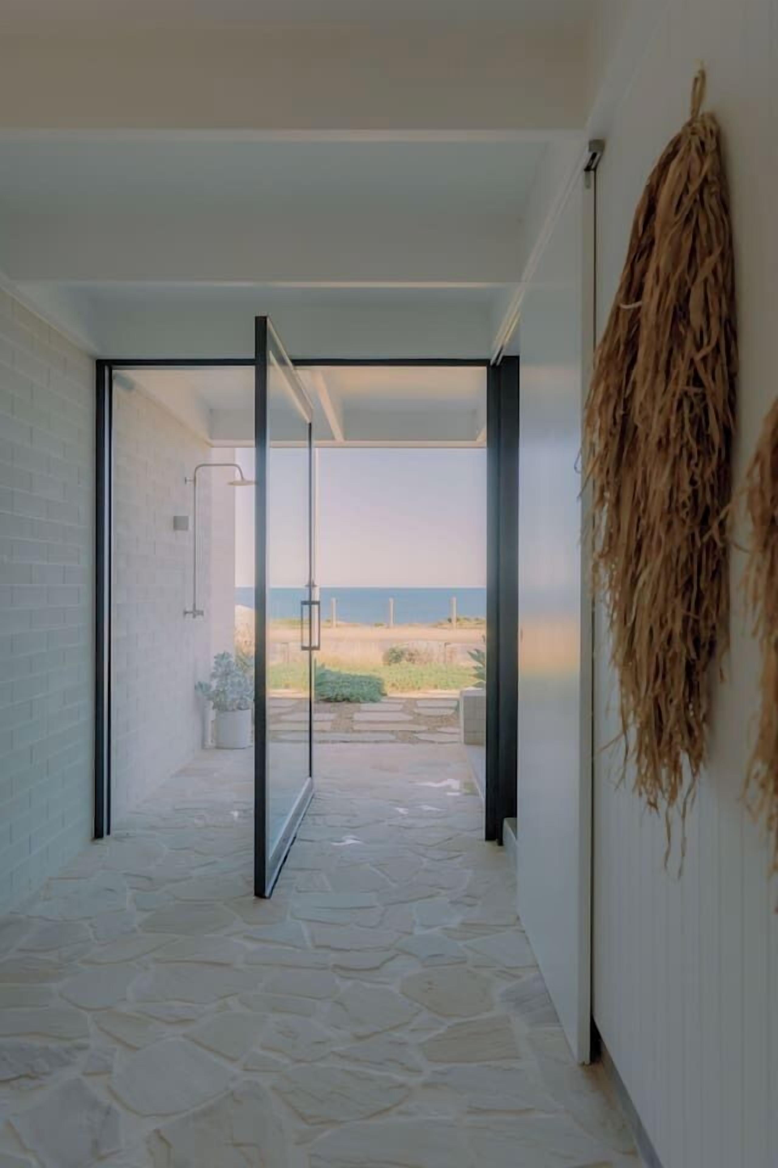 A hallway with a glass door leading to a balcony with a view of the beach.