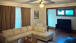 Una sala de estar con un sofá modular, una mesa de centro, un ventilador de techo y vista a un cuarto con televisor.