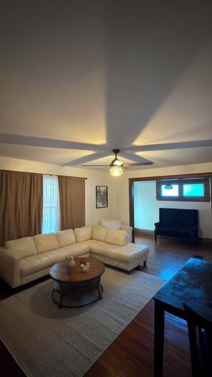 Ein Wohnzimmer mit einem Ecksofa, einem Couchtisch, einem Deckenventilator und Blick auf einen Raum mit einem Fernseher.