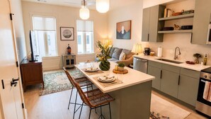 Cozinha moderna com uma ilha central, banquetas, mesa de jantar e um sofá ao fundo.