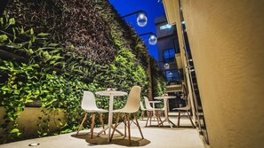 An outdoor seating area with tables and chairs, surrounded by lush greenery and a building in the background. - Alko Hotel Cotona (Santa Marta)