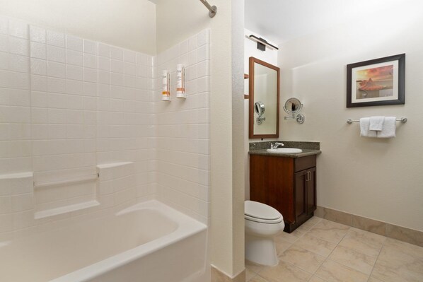 Un baño con bañera, inodoro, lavamanos y un cuadro en la pared.