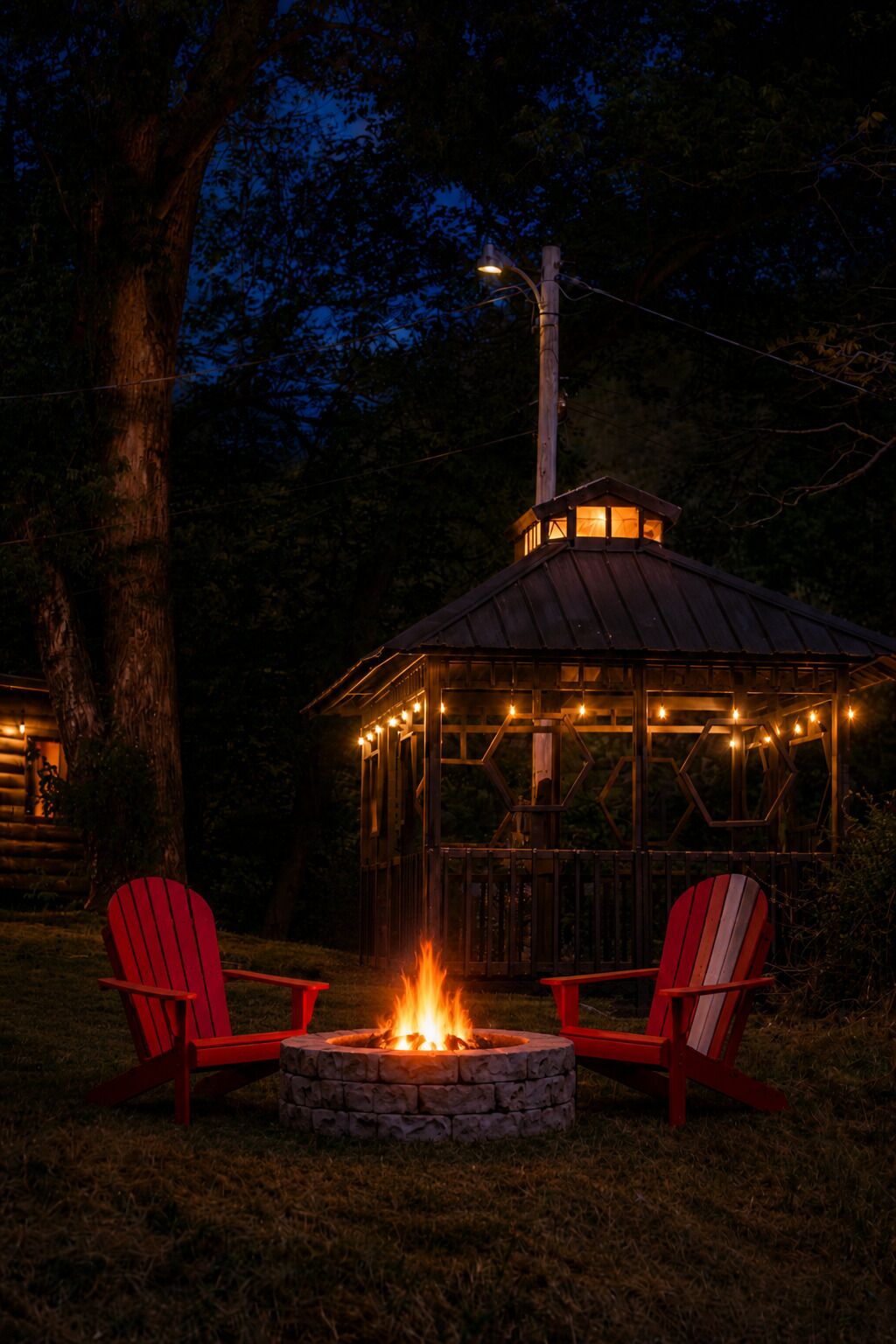 A gazebo with a fire pit, two red Adirondack chairs, and a wooden deck.