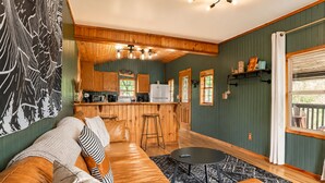 A cozy living room with a leather sofa, a small round table, and a kitchen area with wooden cabinets and a refrigerator. - Onyx at Nada - Your Escape to Nada Tunnel (Stanton)