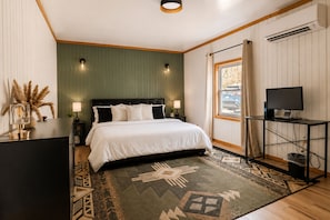 Ein Schlafzimmer mit einem Bett, Nachttischlampen, einem Fernseher, einem Schreibtisch und einem Fenster mit Vorhängen.