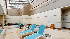 Een binnenzwembad met loungebedden, een pooltafel en een plafondventilator.