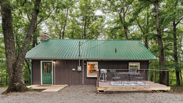 A cabin with a green metal roof, a wooden deck, and a gravel ground.
