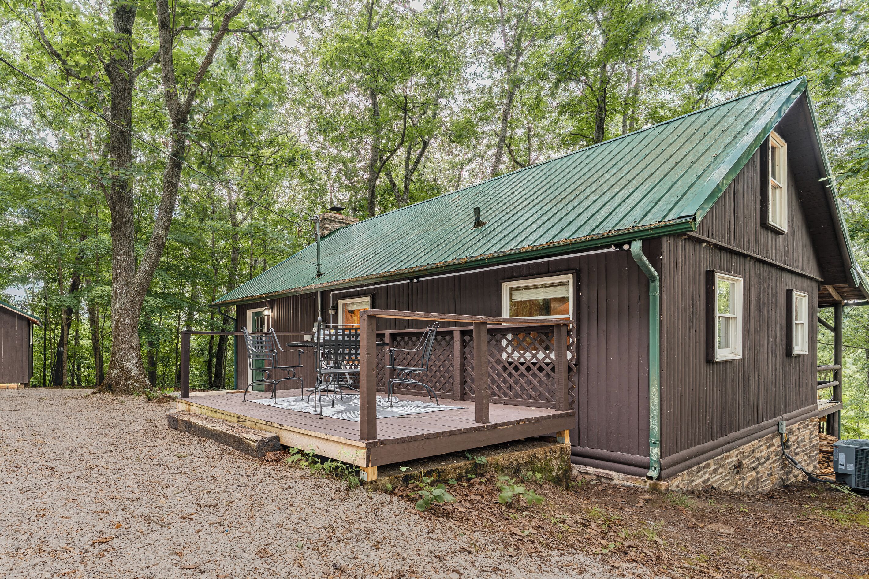 A rustic cabin with a green metal roof, a wooden deck, and a lattice screen.