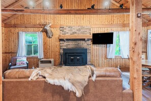 A cozy cabin interior with a fireplace, wooden walls, a sofa, and a mounted animal head. - Social Distance/127 Private Acres -Hot Tub -Wi-Fi (Irvine)