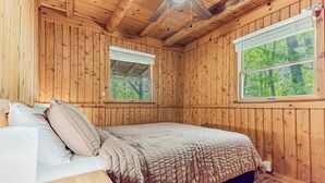 A wooden room with a bed, two windows, and a ceiling fan.